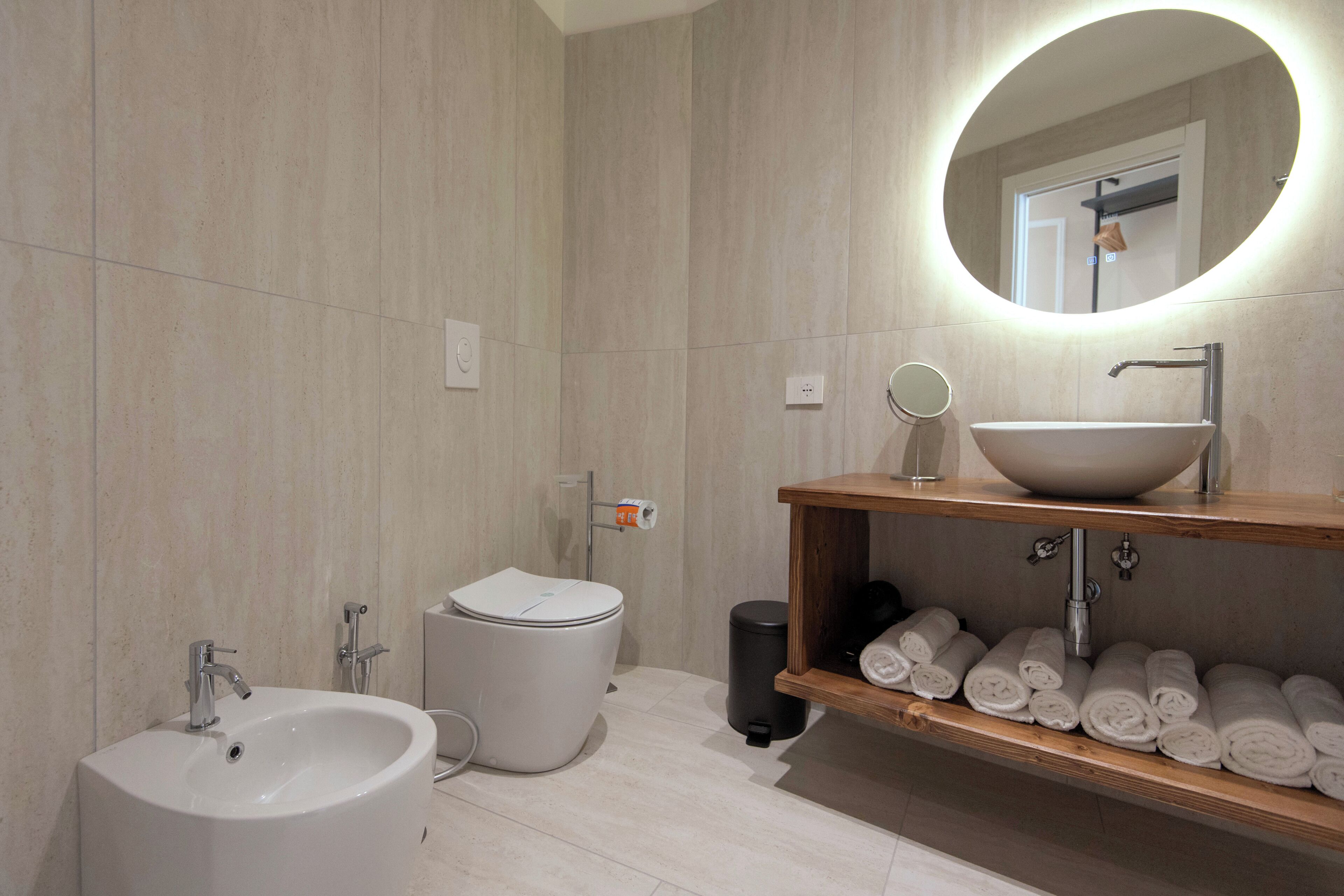 Un baño moderno con lavamanos blanco, inodoro, bidé, espejo y repisa con toallas.