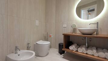 Un baño moderno con lavamanos blanco, inodoro, bidé, espejo y repisa con toallas.