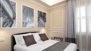 Habitación de hotel con una cama, una silla, una mesita y tres cuadros en la pared.