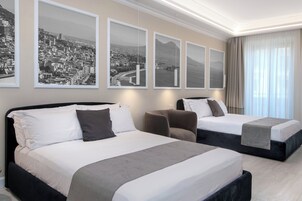 Habitación de hotel con dos camas, una silla y tres cuadros con vistas urbanas en la pared.