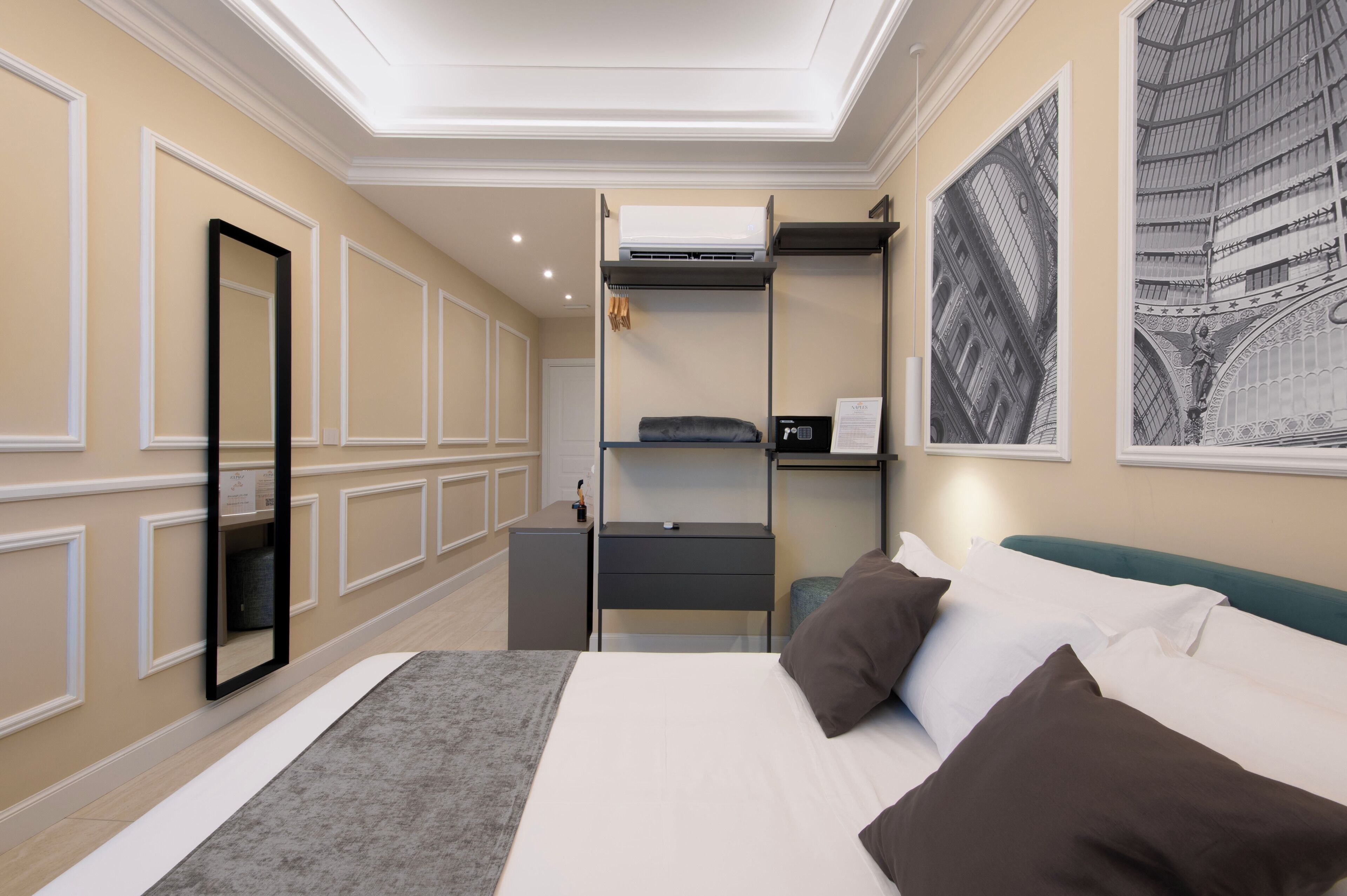 Quarto de hotel com cama, mesa de cabeceira, espelho, guarda-roupa e um quadro grande na parede.