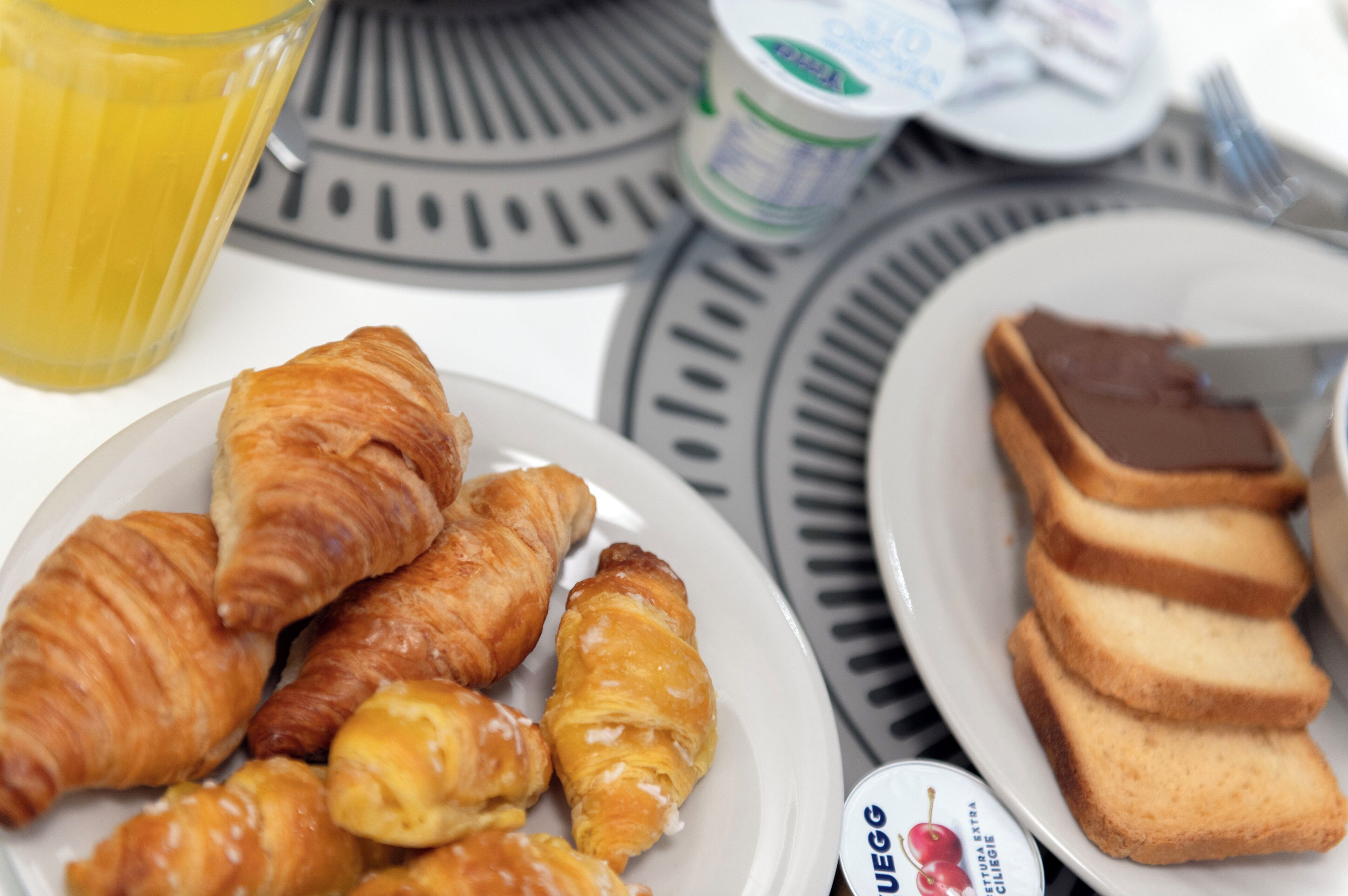 A breakfast setting with croissants, toast, and a juice glass on a table.