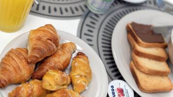 A breakfast setting with croissants, toast, and a juice glass on a table.
