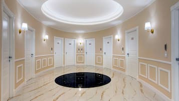 Um saguão de hotel com um detalhe circular preto no chão, paredes em tom de bege e portas brancas.