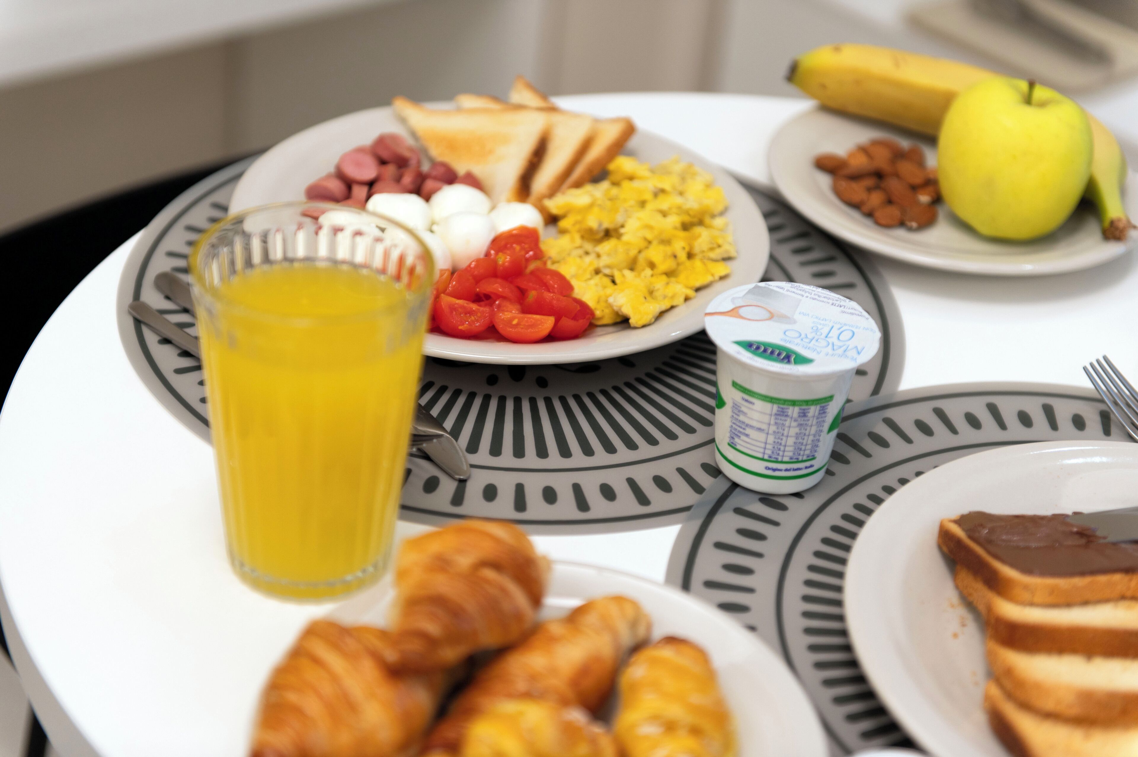 A breakfast table with plates of toast, eggs, tomatoes, and a glass of orange juice.