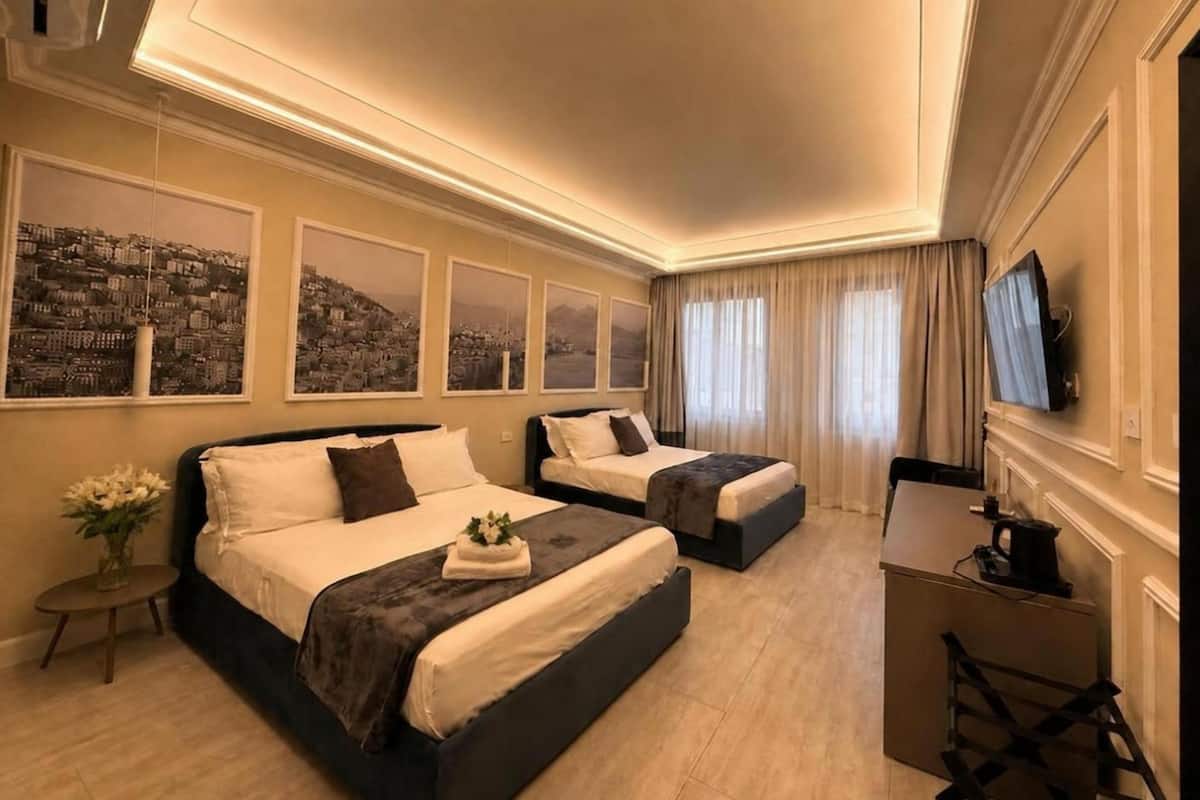 A hotel room with two beds, a desk, a TV, and cityscape artwork on the wall.