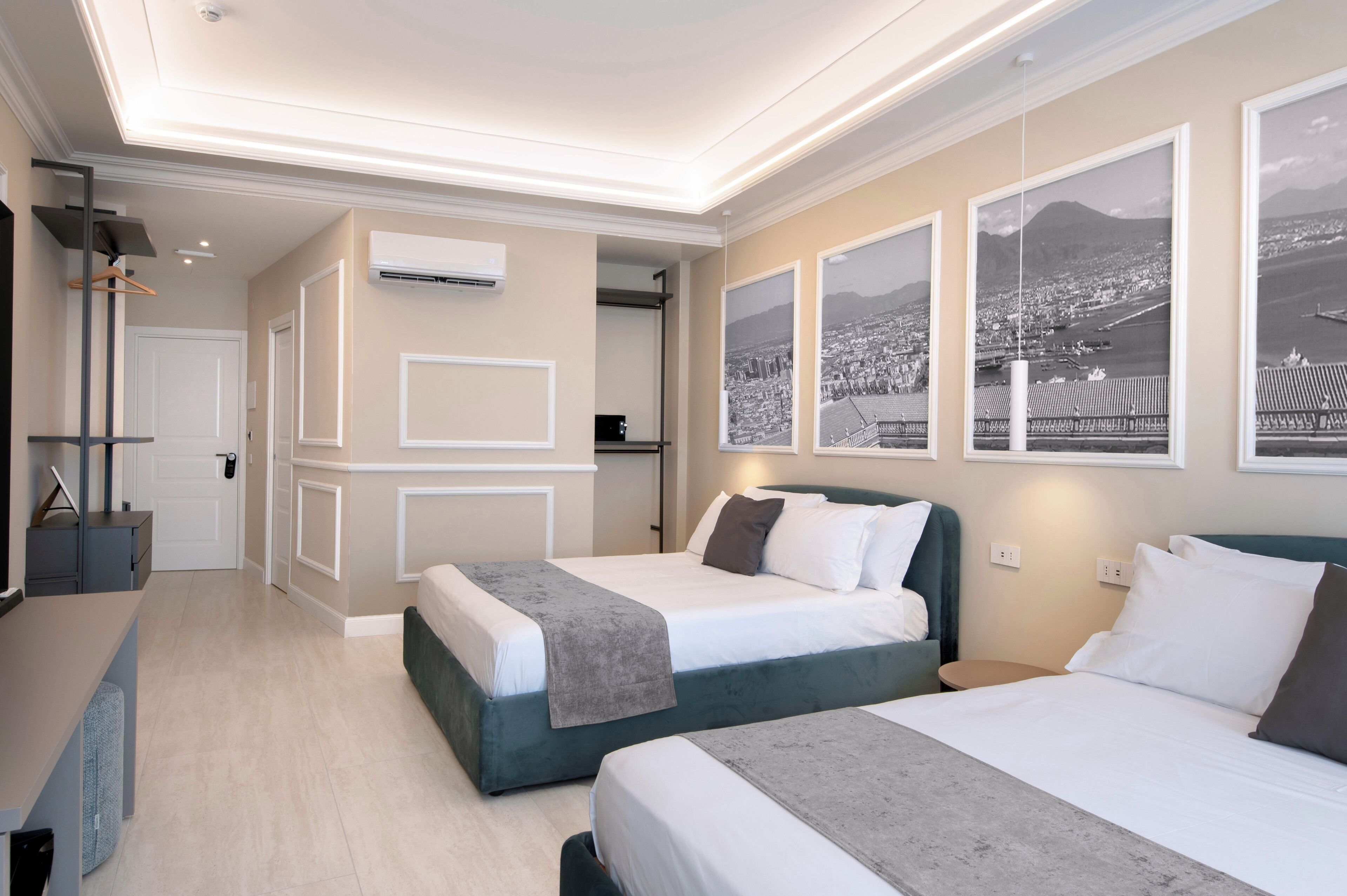 A hotel room with two beds, a desk, a chair, a wardrobe, and a view of a cityscape through the window.