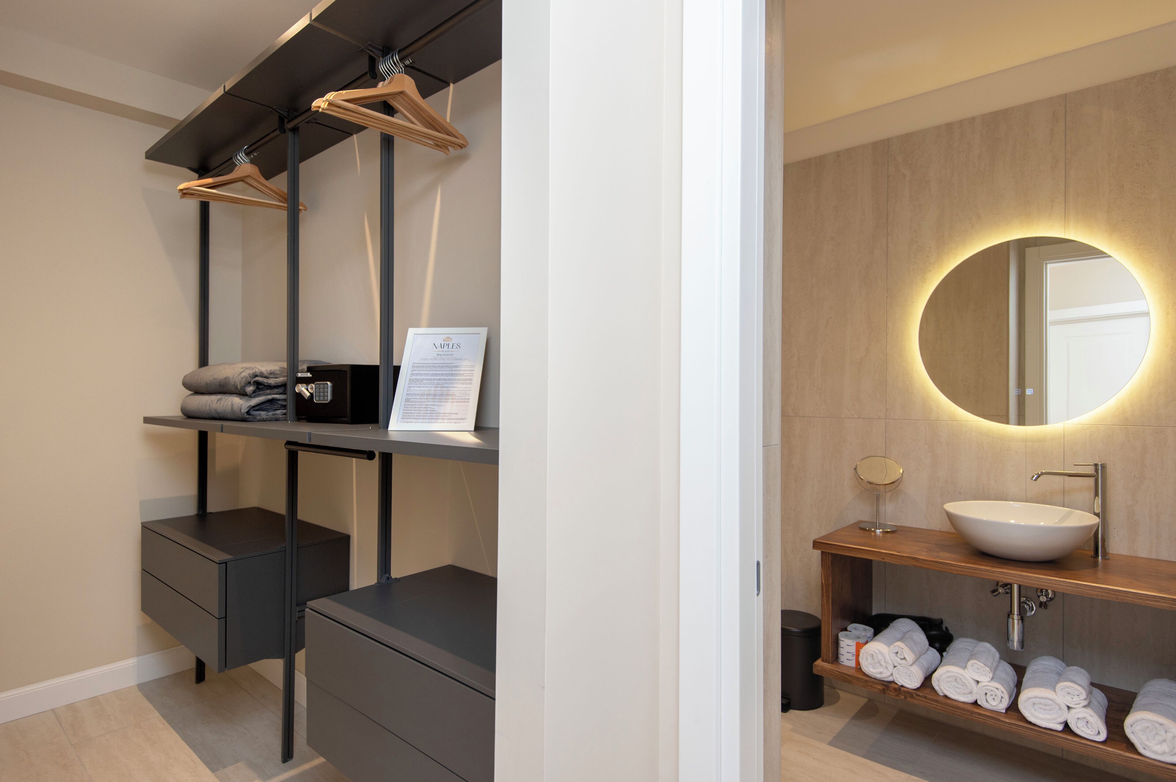 A modern bathroom with a large mirror, a round light, a sink, and neatly folded towels.