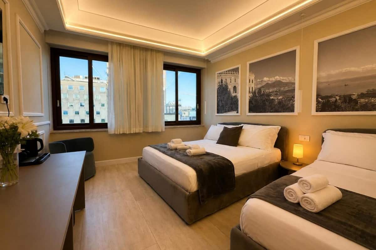 A hotel room with two beds, a desk, and a view of buildings.