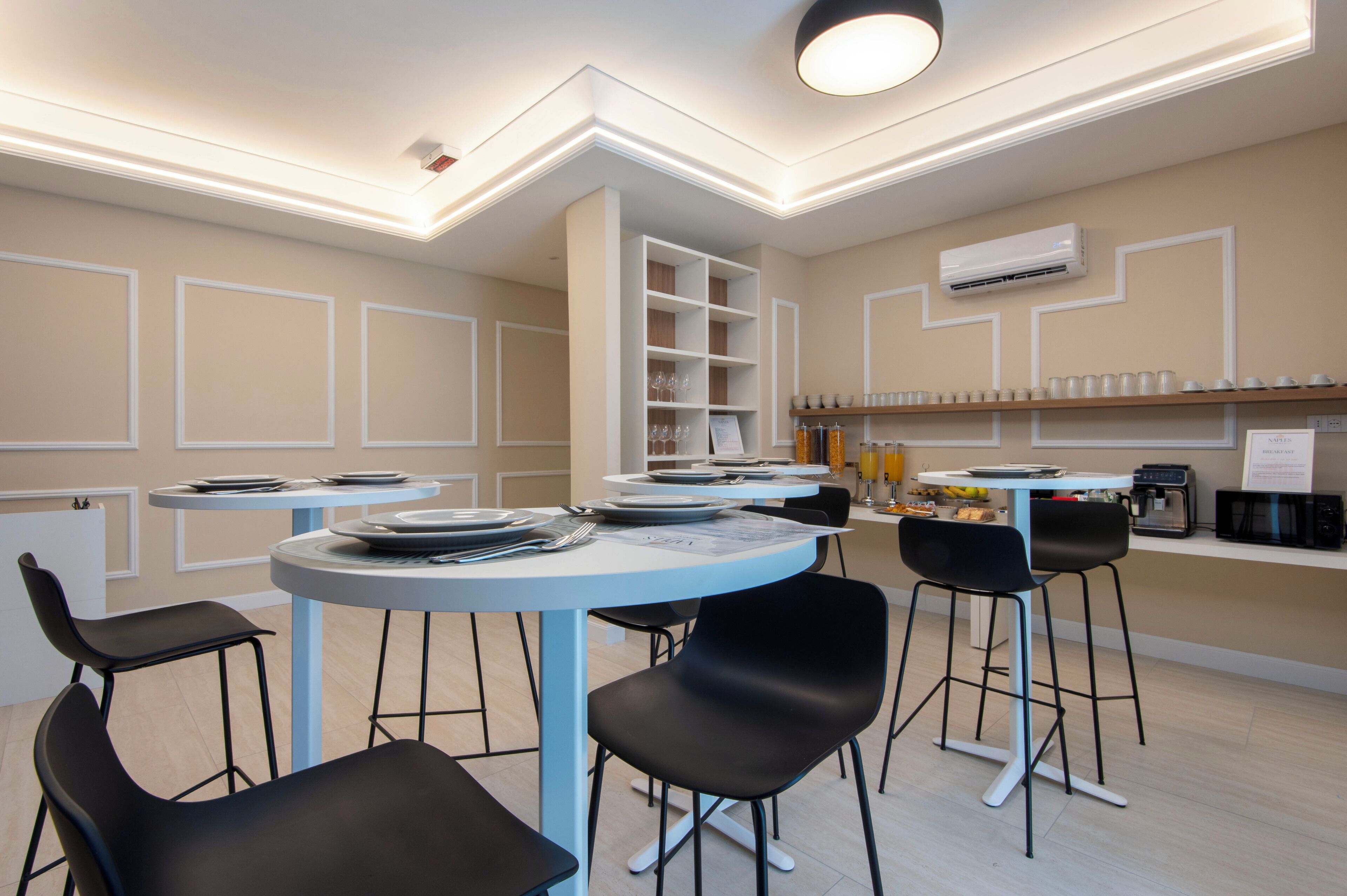Un comedor moderno con mesas redondas, sillas negras y una unidad de estanterías blanca en el centro.