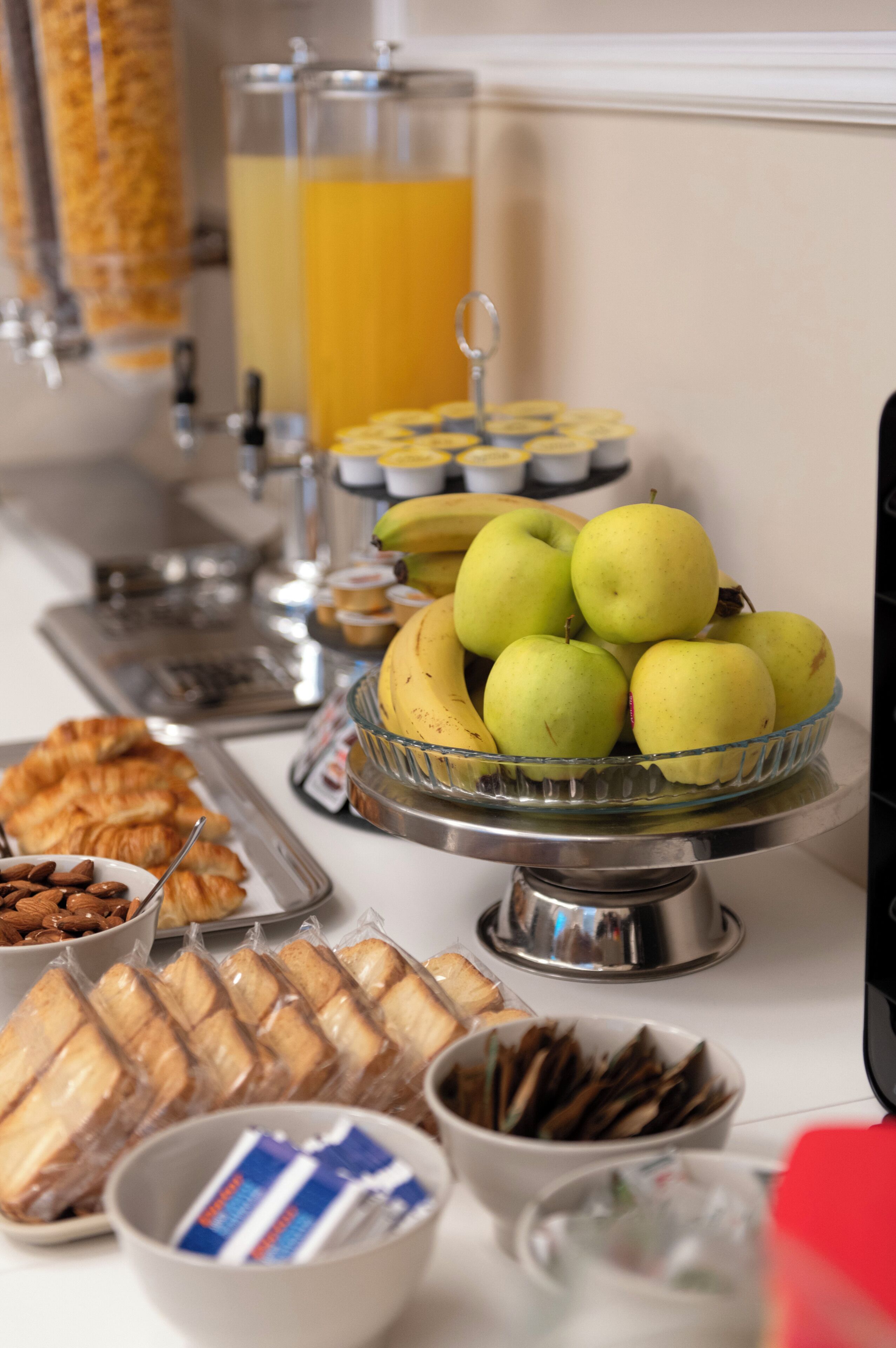 A buffet with various food items including apples, bananas, pastries, and beverages.