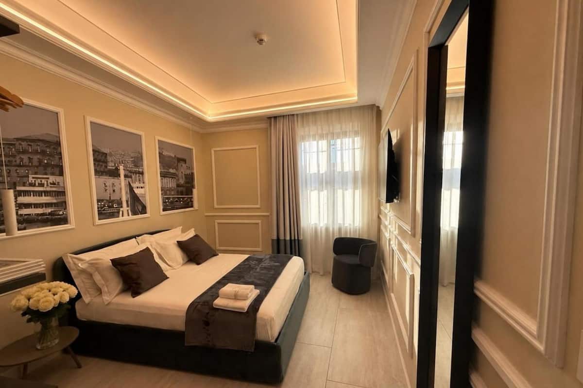 A modern hotel room with a large bed, a desk, a chair, a TV, and a window with curtains.
