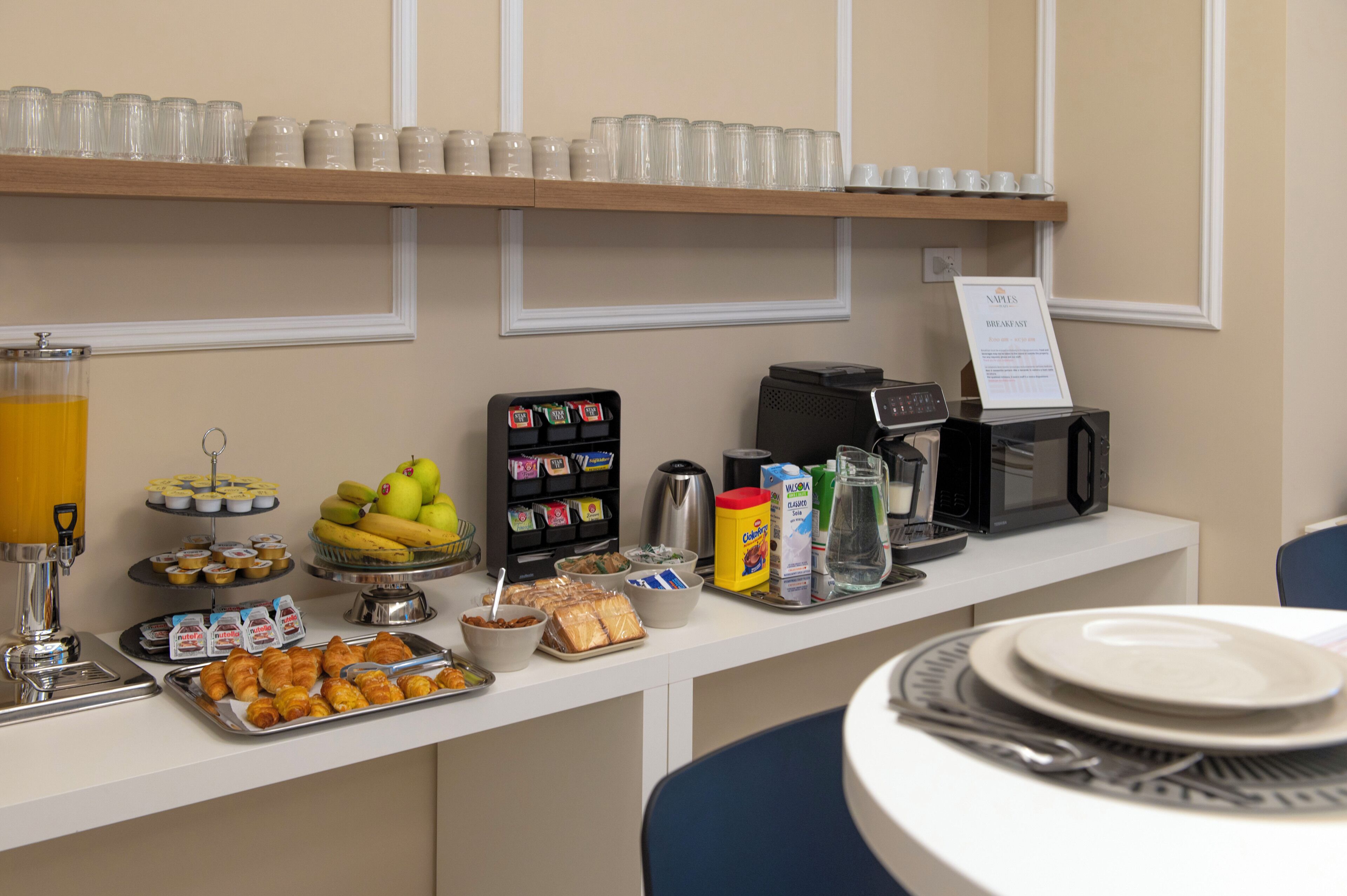 A breakfast buffet with various food items, a coffee machine, and a sign indicating breakfast availability.