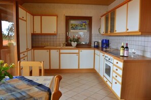 Eine Küche mit Holzausstattung, einer gefliesten Spritzschutzwand, einem Fenster mit einem Gemälde und einem Tisch mit Stühlen.