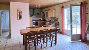 Eine Küche mit Holzschränken, einem Esstisch mit Stühlen, einer Hängelampe und Blick durch eine Glastür.