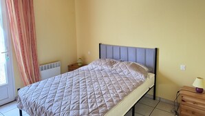 Ein Einzelbett mit gestepptem Kopfteil, ein Nachttisch mit Lampe und ein Fenster mit Vorhängen.