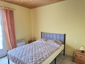 Ein Einzelbett mit gestepptem Kopfteil, ein Nachttisch mit Lampe und ein Fenster mit Vorhängen.