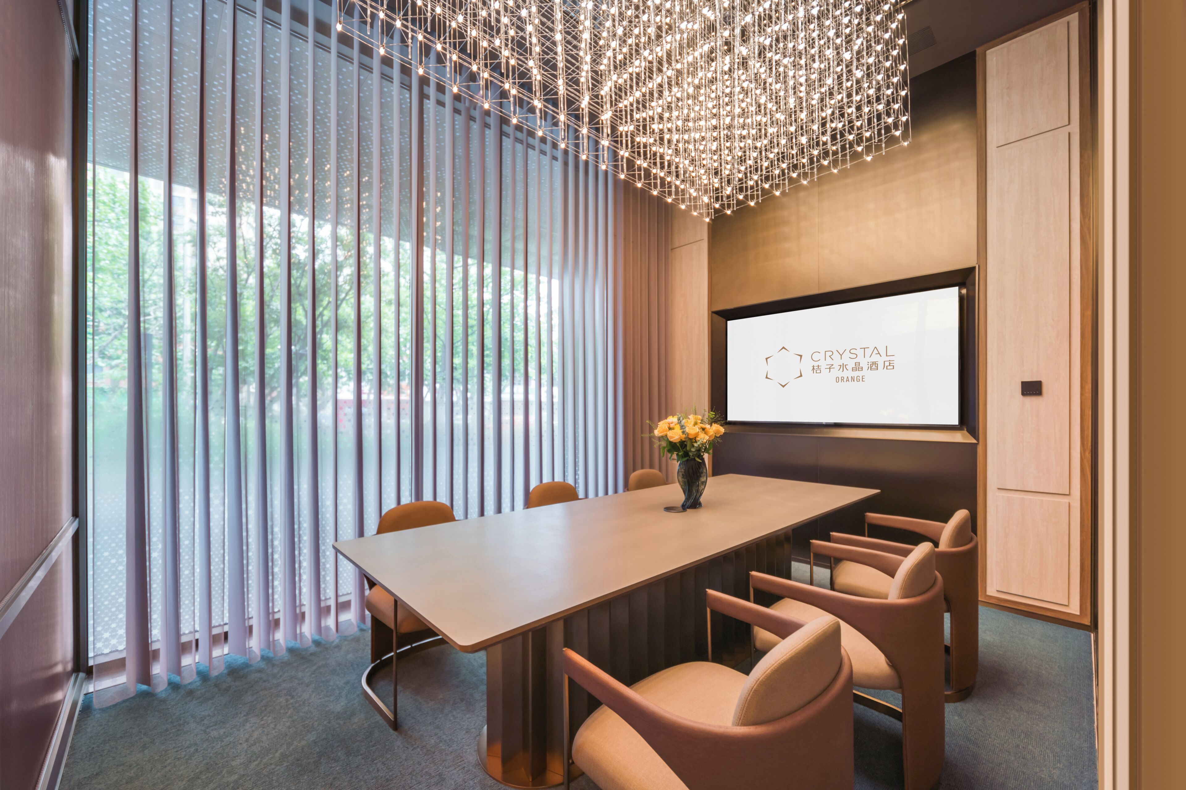 A conference room with a long table, chairs, a projector screen, and a decorative chandelier.