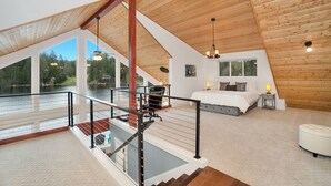 A spacious bedroom with a large window, a wooden ceiling, and a view of a lake. - Modern Lakefront home, 3 bds, 2 baths, dock, gazebo, kayaks, and fishing. (Stanwood)
