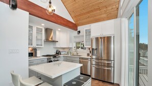 A modern kitchen with white cabinets, stainless steel appliances, and a wooden ceiling. - Modern Lakefront home, 3 bds, 2 baths, dock, gazebo, kayaks, and fishing. (Stanwood)