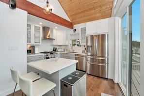 Una cocina moderna con armarios blancos, electrodomésticos de acero inoxidable y techo de madera.
