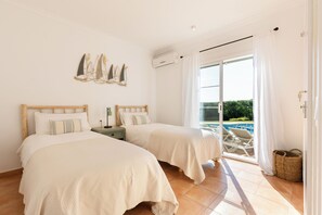 Ein Schlafzimmer mit zwei Betten, einer Schiebetür zu einem Poolbereich und einer Wandklimaanlage.