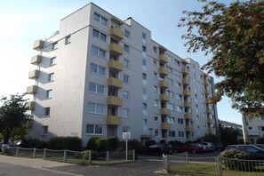 Un immeuble résidentiel à plusieurs étages, doté de balcons, d’une entrée sécurisée et de voitures garées.