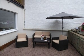 Eine Terrasse mit einer Couch, zwei Stühlen, einem Tisch und einem Sonnenschirm.