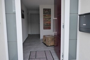 Ein Flur mit Fußmatte, einem Holzschemel und einer Wandleuchte.