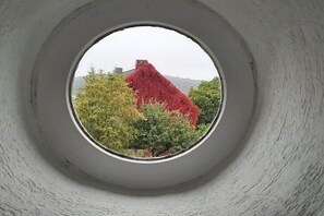 Ein rundes Fenster mit Blick auf eine rote Struktur und Grünflächen.