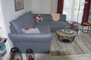 Ein graues Sofa mit einem weißen Kissen, ein Holztisch und ein Teppich mit Muster.