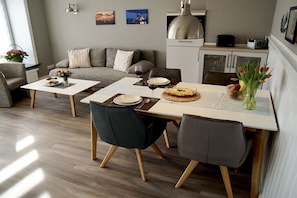 Ein modernes Wohnzimmer mit Esstisch, grauem Sofa und einer Küche im Hintergrund.