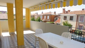 A balcony with a checkered floor, white table and chairs, and yellow-striped awning. - Cozy Vacation Home With Lovely Views in Grado (Grado)