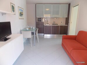 A compact living space with a dining area, kitchenette, and a red sofa. - Cozy Vacation Home With Lovely Views in Grado (Grado)