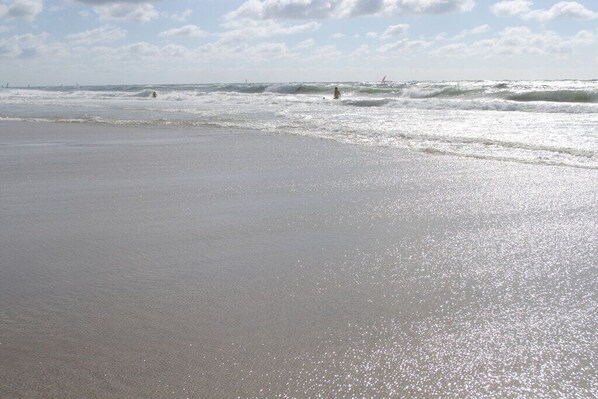 Ein Strand mit Wellen, einem klaren Himmel und einem entfernten Segelboot.