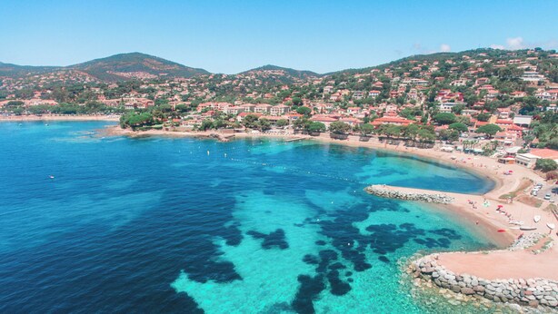 A coastal town with clear turquoise waters, a sandy beach, and a backdrop of red-roofed buildings. - Cosy studio, magnificent swimming pool with exceptional view of the Gulf of St-Tropez (Roquebrune-sur-Argens)