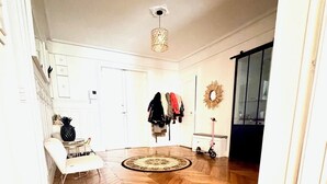 A spacious room with a herringbone wooden floor, a white chair, a coat rack with several coats, and a mirror on the wall. - Champs Elysées  190 m2 - 8 personnes -Exceptionnel Appartement Haussmannien (Paris)