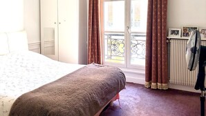 A bedroom with a bed, a wardrobe, a radiator, and a balcony with curtains. - Champs Elysées  190 m2 - 8 personnes -Exceptionnel Appartement Haussmannien (Paris)