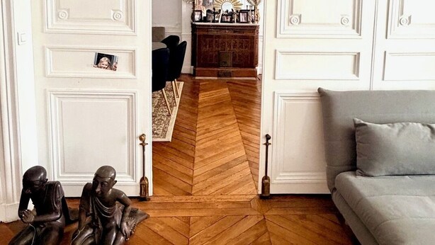 A room with a herringbone floor, a grey sofa, a wooden cabinet, and a mirror with a sunburst frame. - Champs Elysées  190 m2 - 8 personnes -Exceptionnel Appartement Haussmannien (Paris)