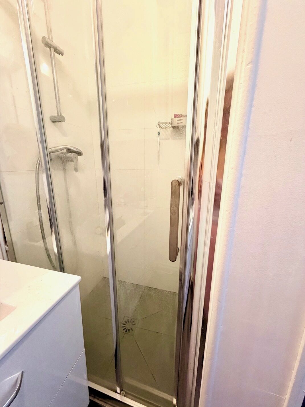 Une douche en verre avec des accessoires chromés, un lavabo blanc et un sol carrelé.