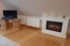 Ein Zimmer mit Kamin, Fernseher auf einem Holzboden und Heizkörper.