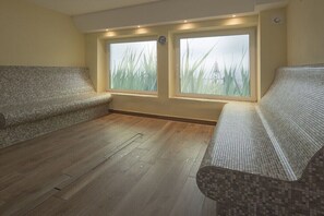 Ein Zimmer mit Holzboden, zwei gemusterten Sofas und großen Fenstern mit Blick auf hohes Gras.