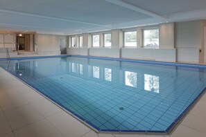 Ein großer Innenpool mit klarem, blauem Wasser, umgeben von weißen Wänden und Fenstern.