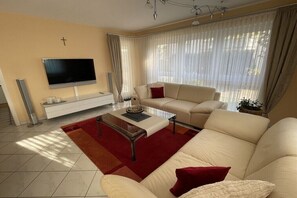 Ein Wohnzimmer mit einer Couch, einem Couchtisch, einem Fernseher und einem Kruzifix an der Wand.