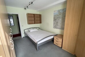 Ein Schlafzimmer mit Bett, Nachttisch, Kleiderschrank und Wandregal.