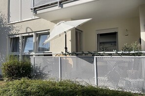 Ein Gebäude mit weißer Fassade, einem Balkon mit weißem Sonnenschirm und einem Metallzaun.