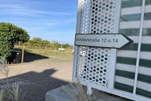 Ein Hinweisschild für 'Schillerstraße 12 u. 14' mit einer Metall-Schichtwand und grün-weiß gestreiftem Hintergrund.
