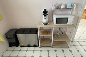 Uma cozinha compacta com cafeteira, micro-ondas e lixeira.