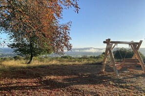 Ein hölzernes Schaukelgerüst in einer natürlichen Umgebung mit Baum und Blick auf eine entfernte Landschaft.