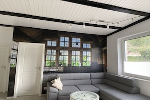 A room with a gray sofa, a white clock, and a window with a view of greenery. - Holiday apartment with 3 bedrooms (Sinzig)